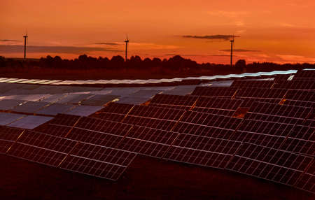 Solar panel field station and silhouettes of wind turbines against the evening sky, the concept of...
