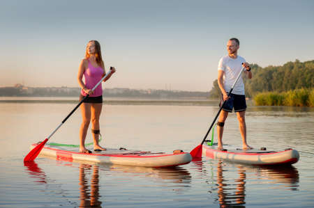 A couple swims together on a stand-up paddleboard, active lovers' recreation, water tourismの写真素材