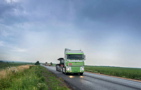 a big truck driving on a rainy wet highway around fields with headlights reflecting on the road,...
