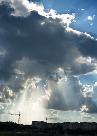 Silhouettes of tower crane and buildings on sunset sky with clouds and sun rays backgroundの写真素材