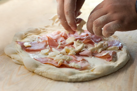 chef's hands placing ham and cheese on pizza dough