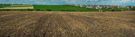 plowed field, green-yellow stripes of grain fields on the horizon, agricultural land, cumulus clouds in the skyの写真素材
