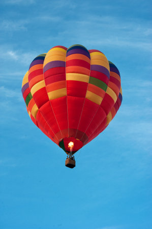 Multicolored bright balloon with basket in blue sky. Fire heats the air in the domeの写真素材