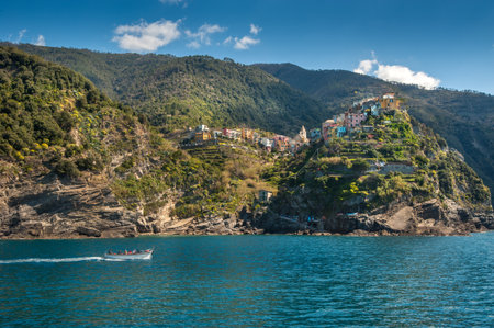 colorful buildings on a cliff between terraced hills, Corniglia , Cinque Terre, boat on the blue waters of the Ligurian Sea.の写真素材