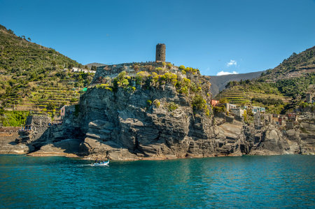 The seaside village on rocks of Vernazza, Cinque Terre, towers of a medieval fortress, and colorful...