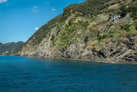 The coast of Cinque Terre green terraces on the slopes. A calm bay with a sailboat near the rocky shoreの写真素材