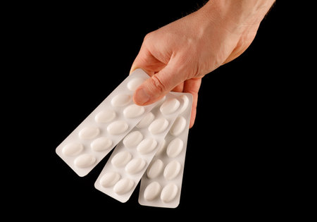 Medication in pills blister in hand on black isolate background