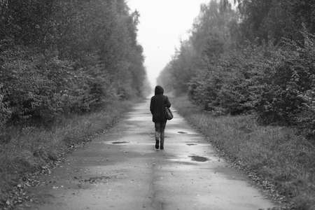 A lonely woman walks on the road in black and whiteの写真素材