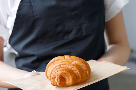 Cafe seller holds a croissant on a tray