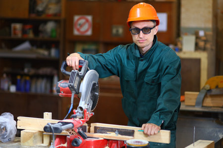 A young and handsome worker man in a helmet and glasses works at the machineの写真素材