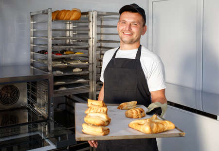 A young baker worker in a bakery is holding pastriesの写真素材
