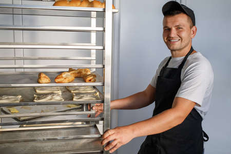A young baker pulls a shelf with pastries in the bakery