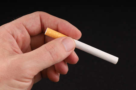 Hand holds a cigarette on a dark backgroundの写真素材