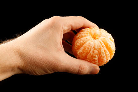 Peeled tangerine in hand isolate on a black backgroundの写真素材