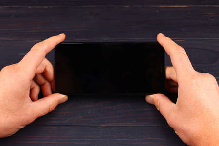 Hands holding smartphone on dark wooden backgroundの写真素材
