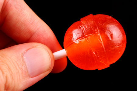 red candy in hand on a stick on black backgroundの写真素材