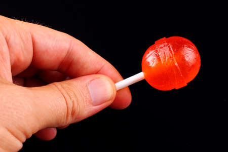 red candy in hand on a stick on black backgroundの写真素材
