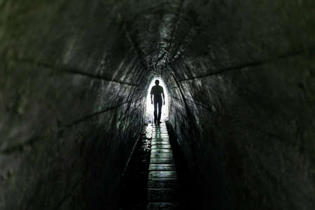 Lonely passerby man in a dark tunnel. Light at the end of the tunnel.の写真素材