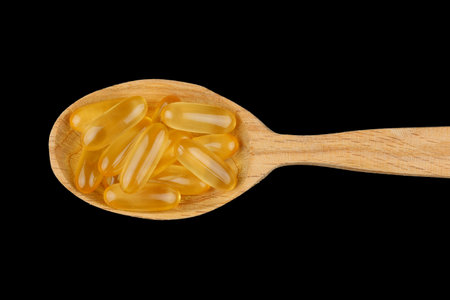 Omega 3 gelatin capsules in a wooden spoon on a black background Top viewの写真素材