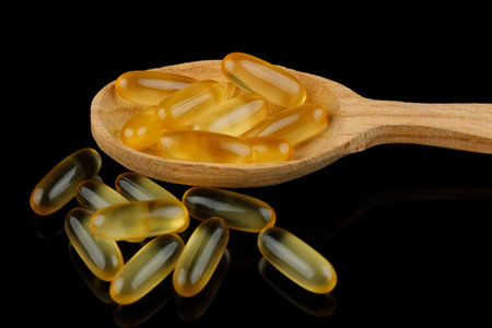 Omega 3 gelatin capsules in a wooden spoon on a black backgroundの写真素材