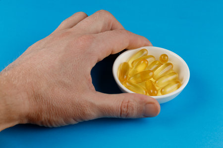 Omega 3 gelatin capsules in a white container in his handの写真素材