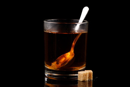 A glass of tea with pieces of sugar on a black backgroundの写真素材
