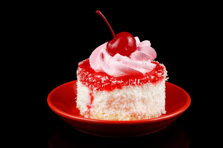 Cake with cream and cherry on a red saucerの写真素材