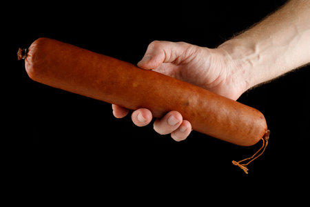 Sausage stick in hand isolated on blackの写真素材