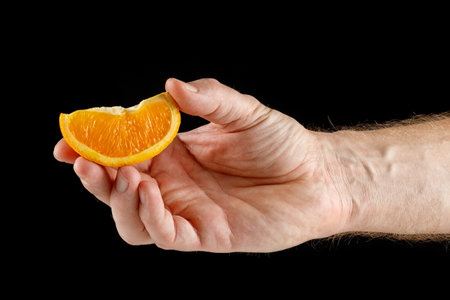 Piece of orange in hand isolated on blackの写真素材
