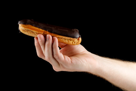 Hand holding eclair on black isolateの写真素材