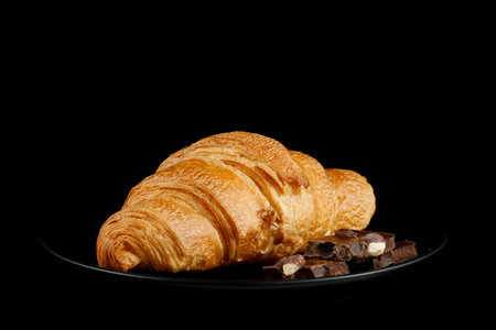 Croissant with pieces of chocolate on a black plate.の写真素材