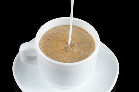 Coffee with milk. Milk is poured into a cup with coffee. White cup of coffeeの写真素材