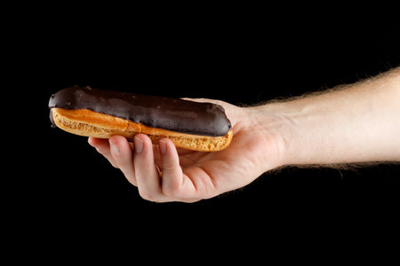 Hand holding eclair on black isolateの写真素材