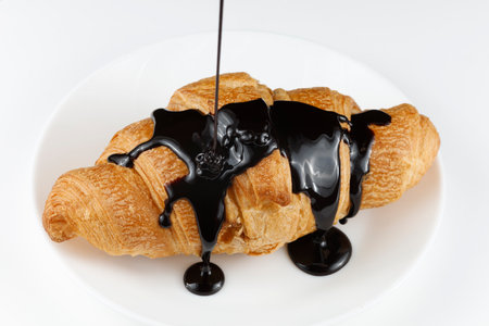 Chocolate poured on croissant close-up. Chocolate with a croissant on a plate.の写真素材