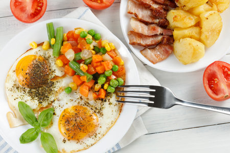 Fried eggs with vegetables, fried bacon and potatoes. Hearty food and a delicious lunch.の写真素材