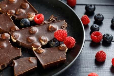 Pieces of chocolate with nuts and berries in a black plateの写真素材