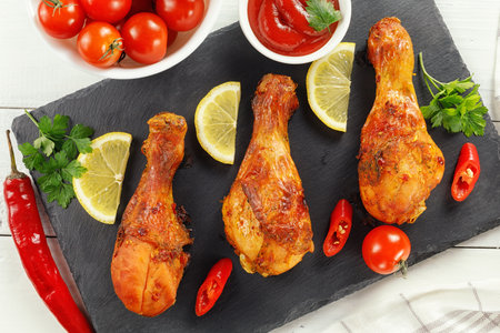 Fried chicken legs with tomatoes and lemon. Grilled spicy chicken legs on a black background.Top view.の写真素材