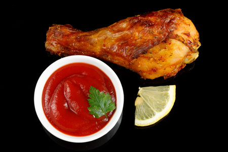 Fried chicken leg with sauce and lemon on black.の写真素材