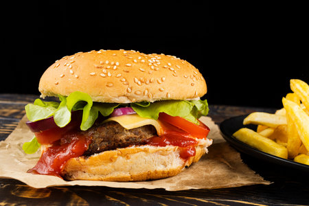 Burger with cutlet, tomato, cheese and greens. Fresh tasty burger isolated on black backgroundの写真素材
