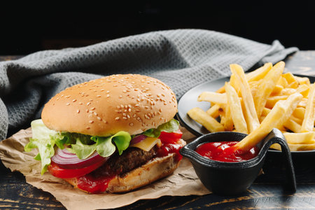 Burger with sauce and french fries. beef burger with cheese, bacon, leafs, onion and french fries on wood tableの写真素材
