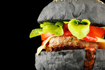 Black burger close-up. Burger with tomatoes, greens, onions and meat. place for text cope spaceの写真素材
