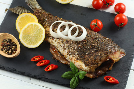 Fried carp fish with vegetables, tomatoes and lemon. Fish baked with vegetablesの写真素材