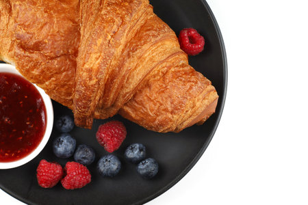 Croissant with jam and berries on a black plate. traditional breakfast.の写真素材