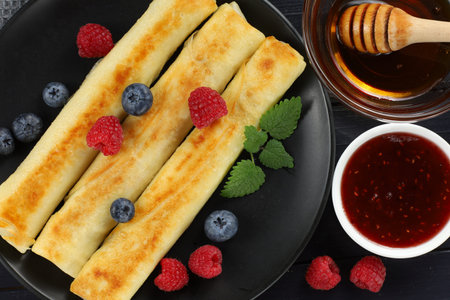 Pancakes rolls with honey and berries. Traditional thin pancakes or crepes with honey and raspberriesの写真素材