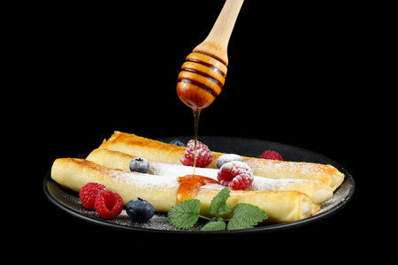 Pancakes rolls with honey and berries. Traditional thin pancakes or crepes with honey and raspberriesの写真素材