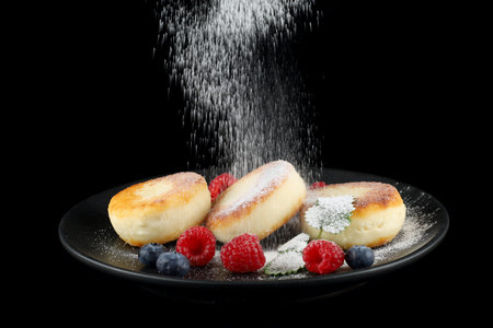 Cottage cheese fritters in a plate with berries. Powdered sugar is sprinkled.の写真素材