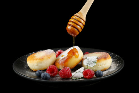 Cottage cheese fritters in a plate with berries. Homemade cheese pancakes with fresh berries and honey. Honey stick with honey.の写真素材