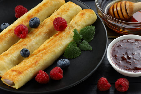 Pancakes rolls with honey and berries. Traditional thin pancakes or crepes with honey and raspberriesの写真素材