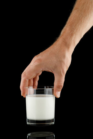 Glass of milk in hand on black isolateの写真素材