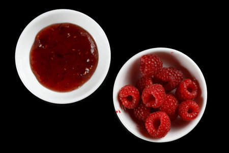 raspberries and jam on black. Jar with delicious raspberry jamの写真素材